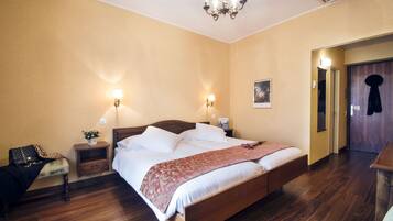 A hotel room with a wooden bed, bedside lamps, a nightstand, a chair, and a door.