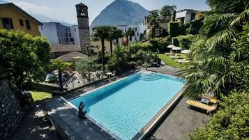 A rectangular swimming pool with a stone deck, surrounded by lush greenery and a mountain in the background.