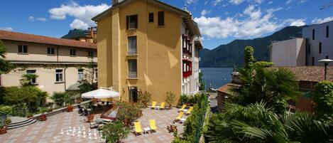 A yellow building with a balcony, a courtyard with chess pieces, and a view of the sea.
