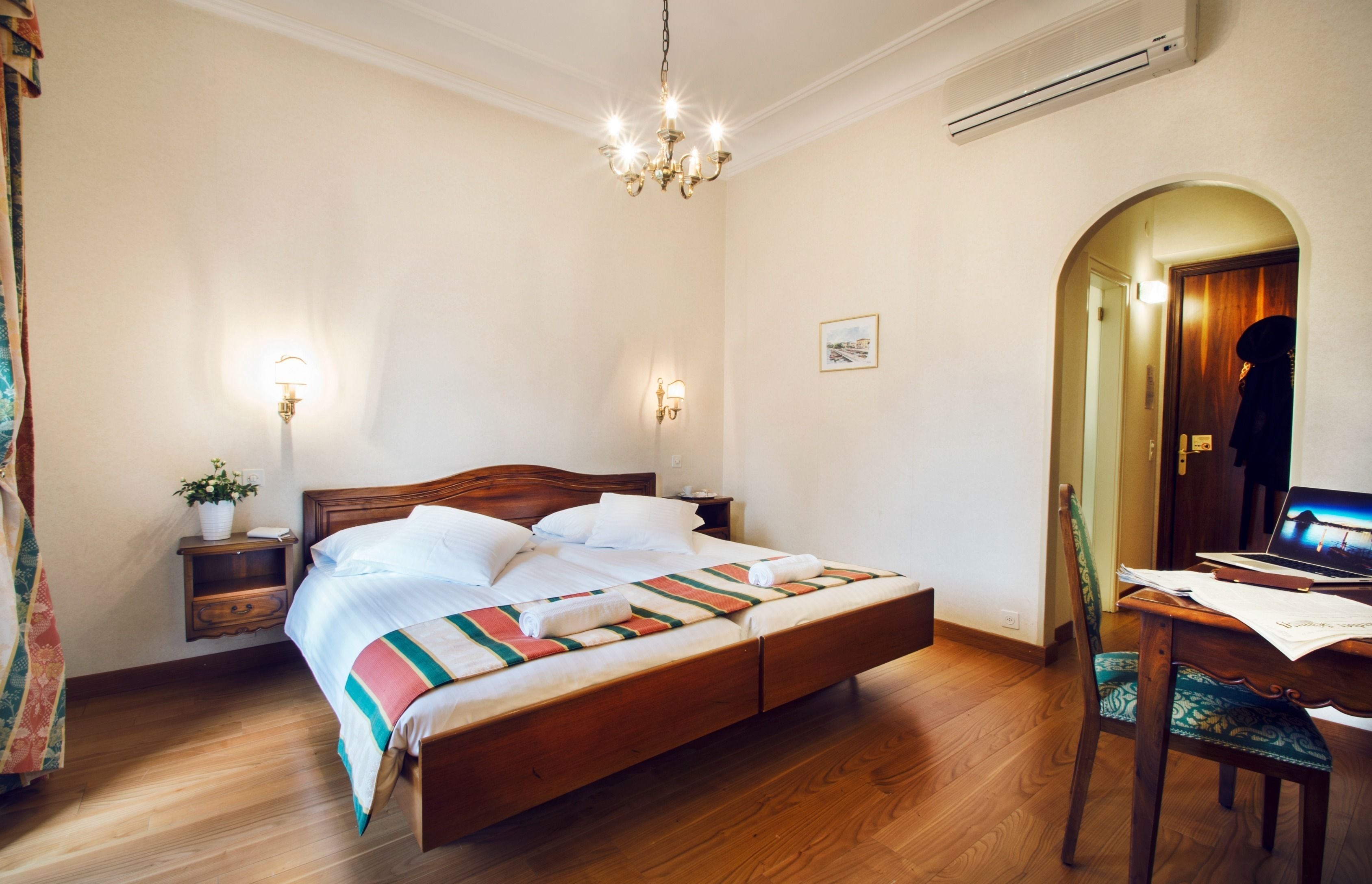 Una camera da letto con un letto di legno, lampade sui comodini, una scrivania con un portatile e una porta ad arco.
