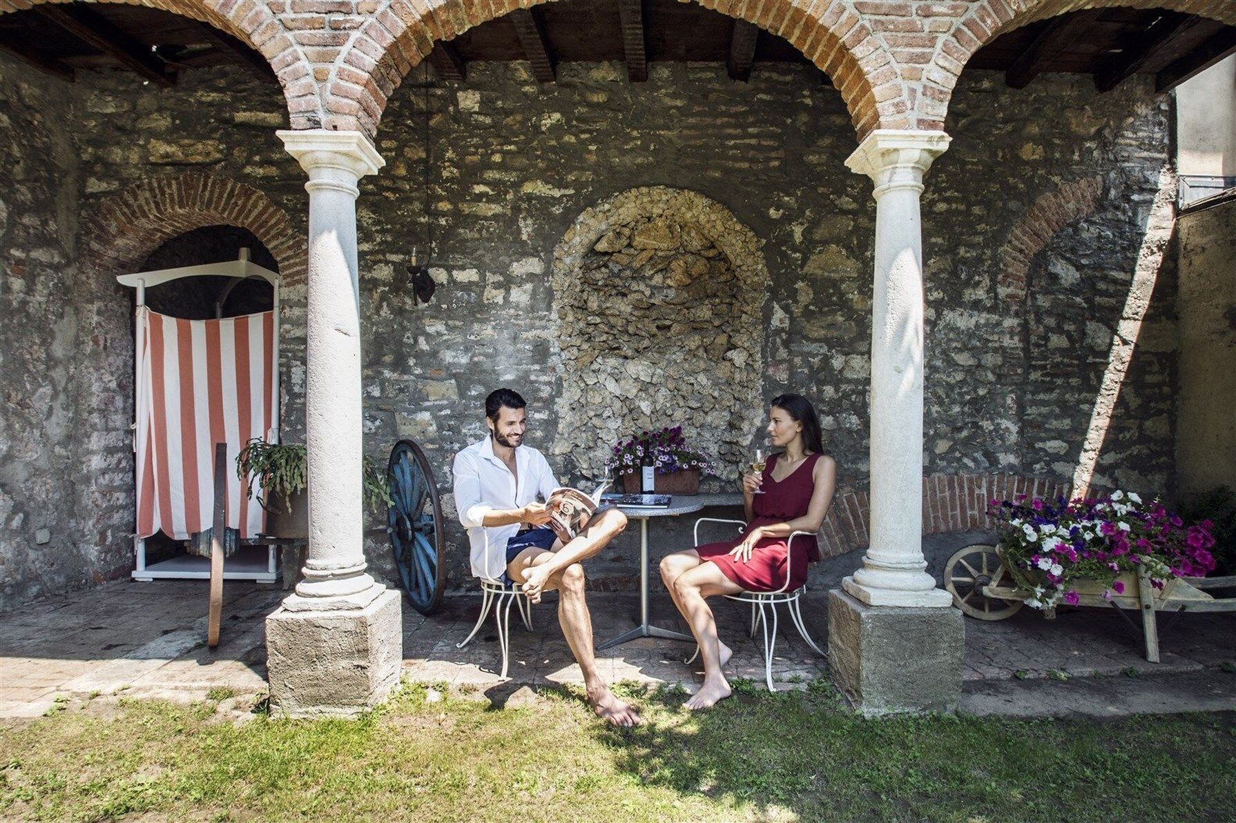 Une cour pavée de pierres, agrémentée d’arcades, d’un auvent à rayures et d’une table avec des chaises.
