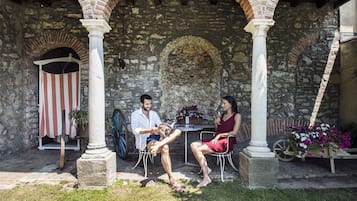 Une cour pavée de pierres, agrémentée d’arcades, d’un auvent à rayures et d’une table avec des chaises.
