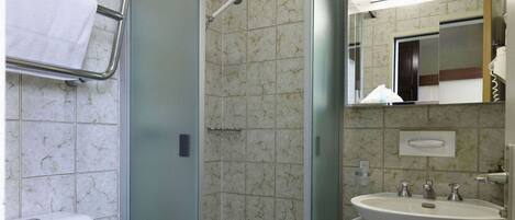 A bathroom with a toilet, a shower enclosure, a sink, and a mirror.