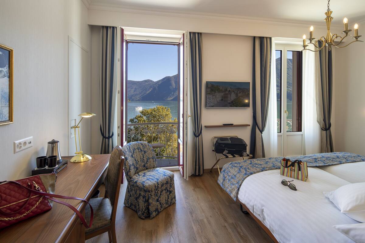 Une chambre d’hôtel avec un bureau en bois, deux chaises, un lit, une télévision et une vue sur les montagnes.