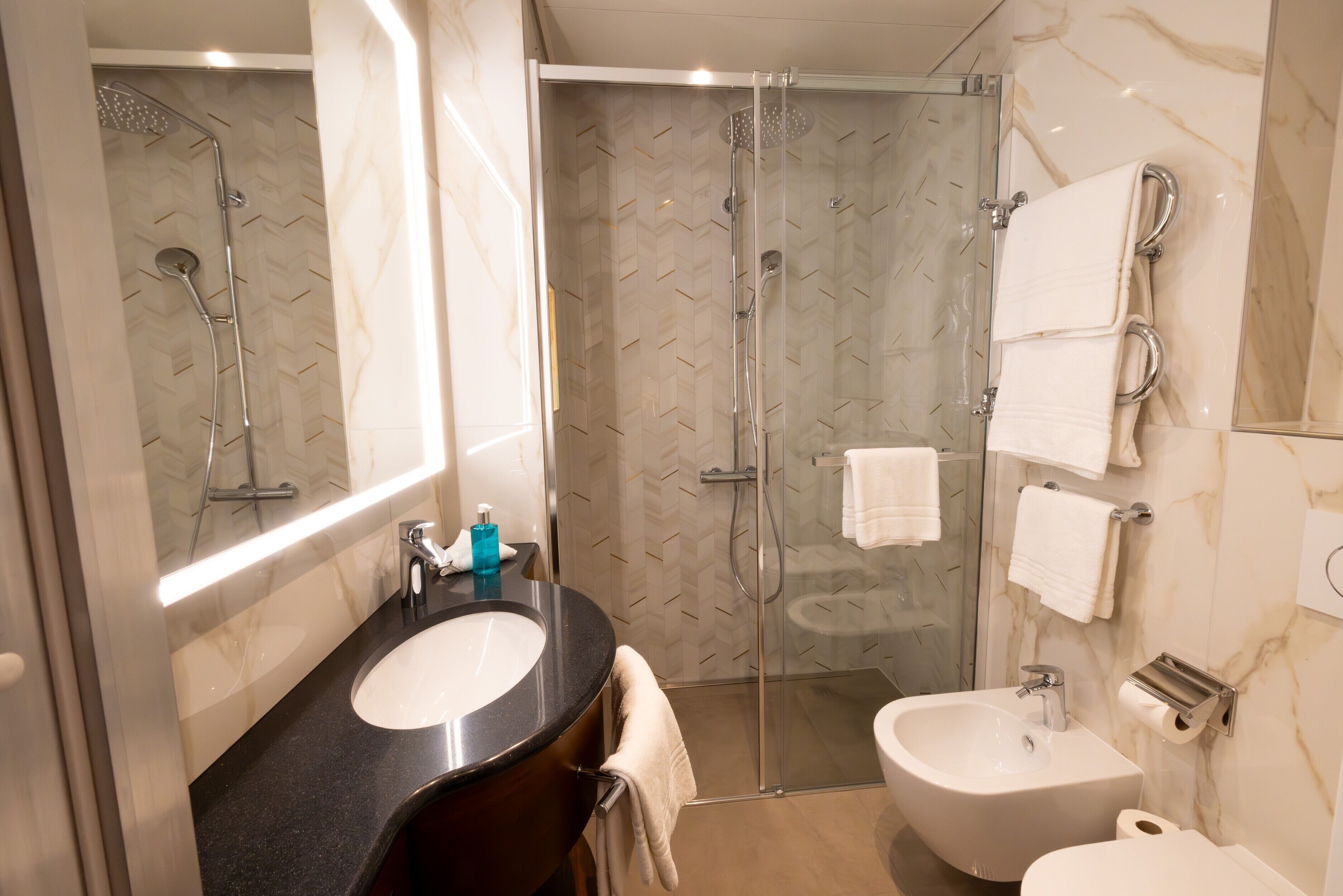 A modern bathroom with a glass-enclosed shower, a large mirror, a black countertop, a sink, and a bidet.