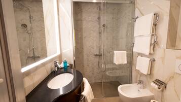 A modern bathroom with a glass-enclosed shower, a large mirror, a black countertop, a sink, and a bidet.