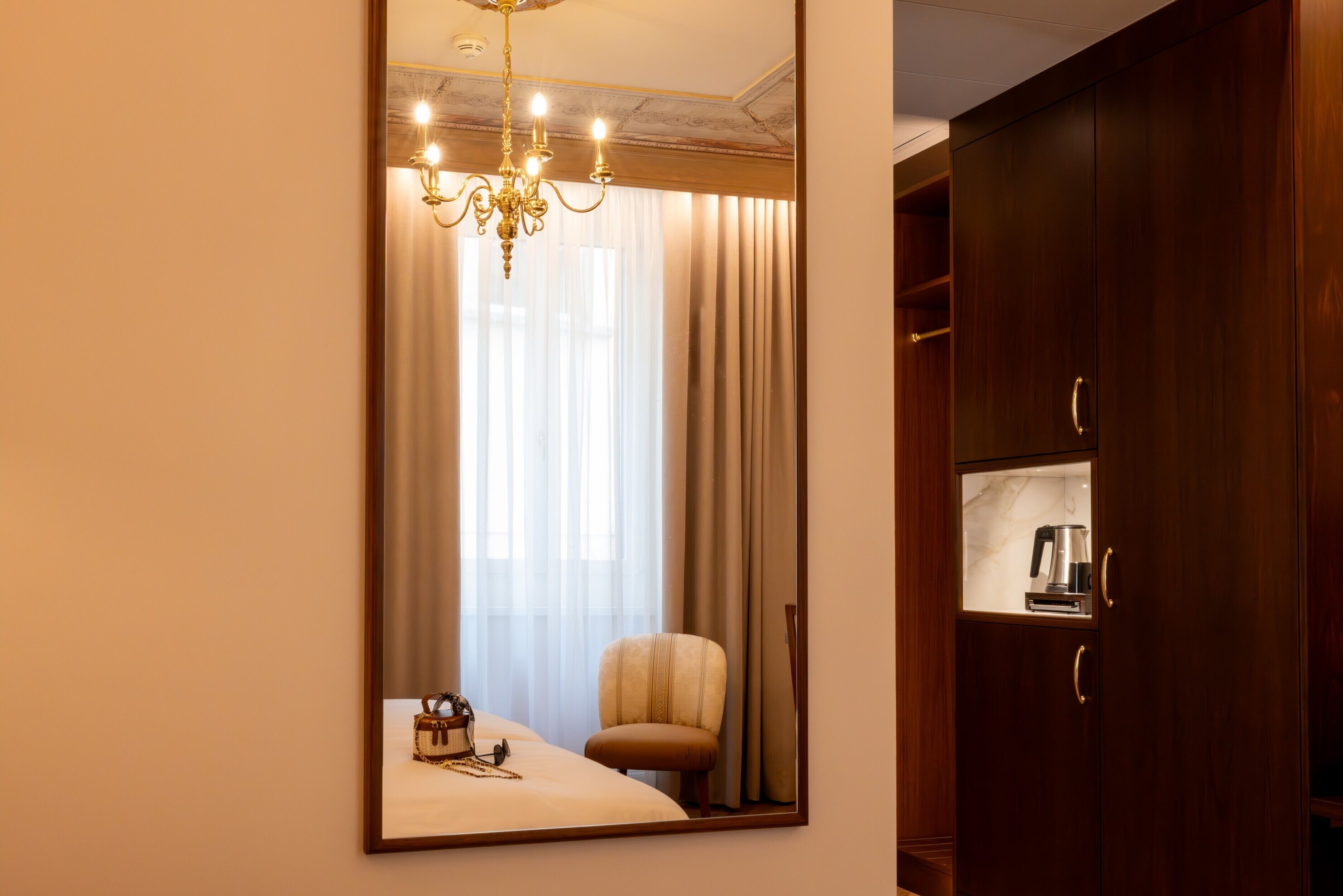 Une chambre à coucher avec un grand miroir, un lit, une chaise, un lustre et une armoire.