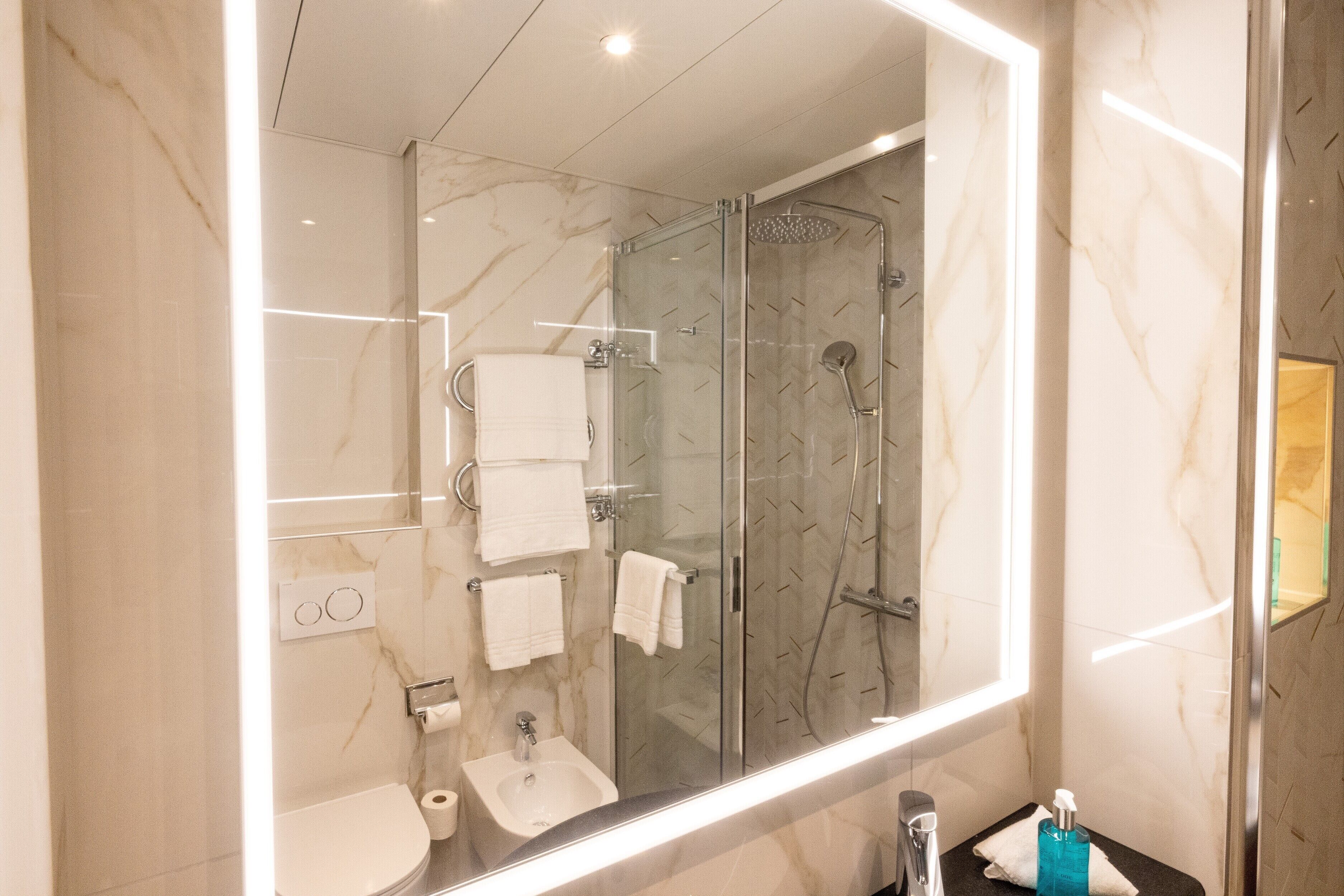 Un baño moderno con ducha envuelta en vidrio, un espejo grande y paredes de mármol.