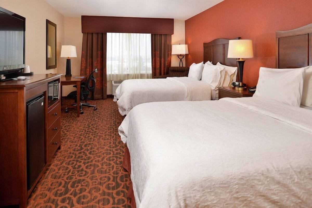A hotel room with two beds, a desk with a chair, a TV, and a minibar.