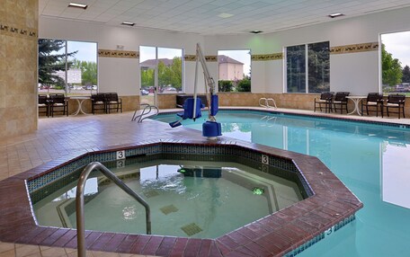 An indoor swimming pool with a hot tub, seating area, and large windows.