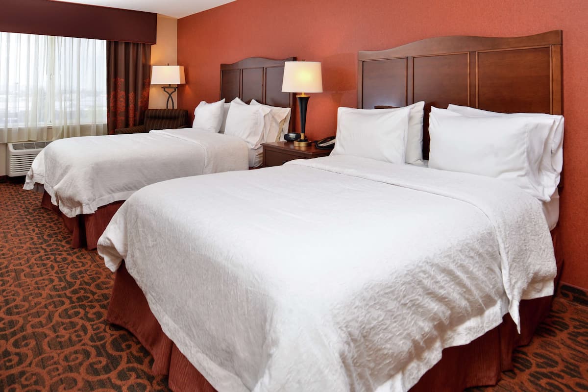 A hotel room with two beds, a large window with curtains, a patterned carpet, and a wooden headboard.