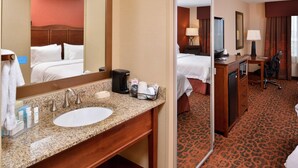 A hotel room with a large bed, a bathroom with a sink and mirror, a desk with a chair, and a carpeted floor. - Hampton Inn Idaho Falls/Airport (Idaho Falls)