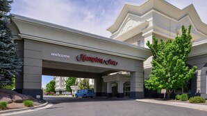 A hotel entrance with a 'Welcome Hampton Inn' sign, a parking area, and a tree in front. - Hampton Inn Idaho Falls/Airport (Idaho Falls)