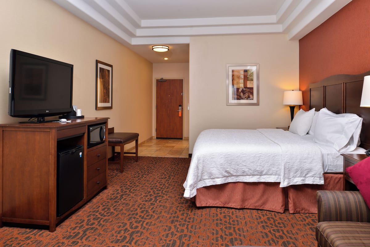 A hotel room with a bed, a desk with a television, a chair, and a door leading to another room.