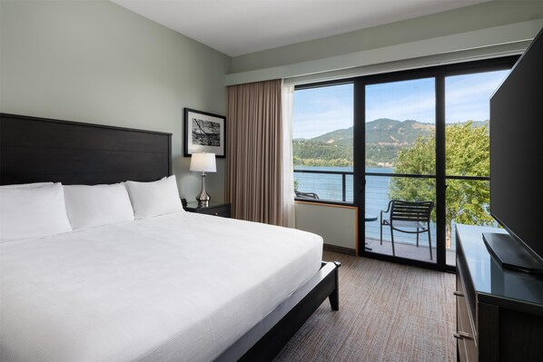 A hotel room with a large bed, a desk with a flat-screen TV, a chair, and a balcony with a scenic view of hills and a lake. - Best Western Plus Hood River Inn (Hood River)