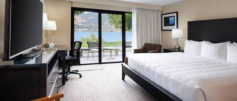 Habitación de hotel con una cama grande, un escritorio con televisor, una silla, una lámpara de escritorio y vistas al exterior.