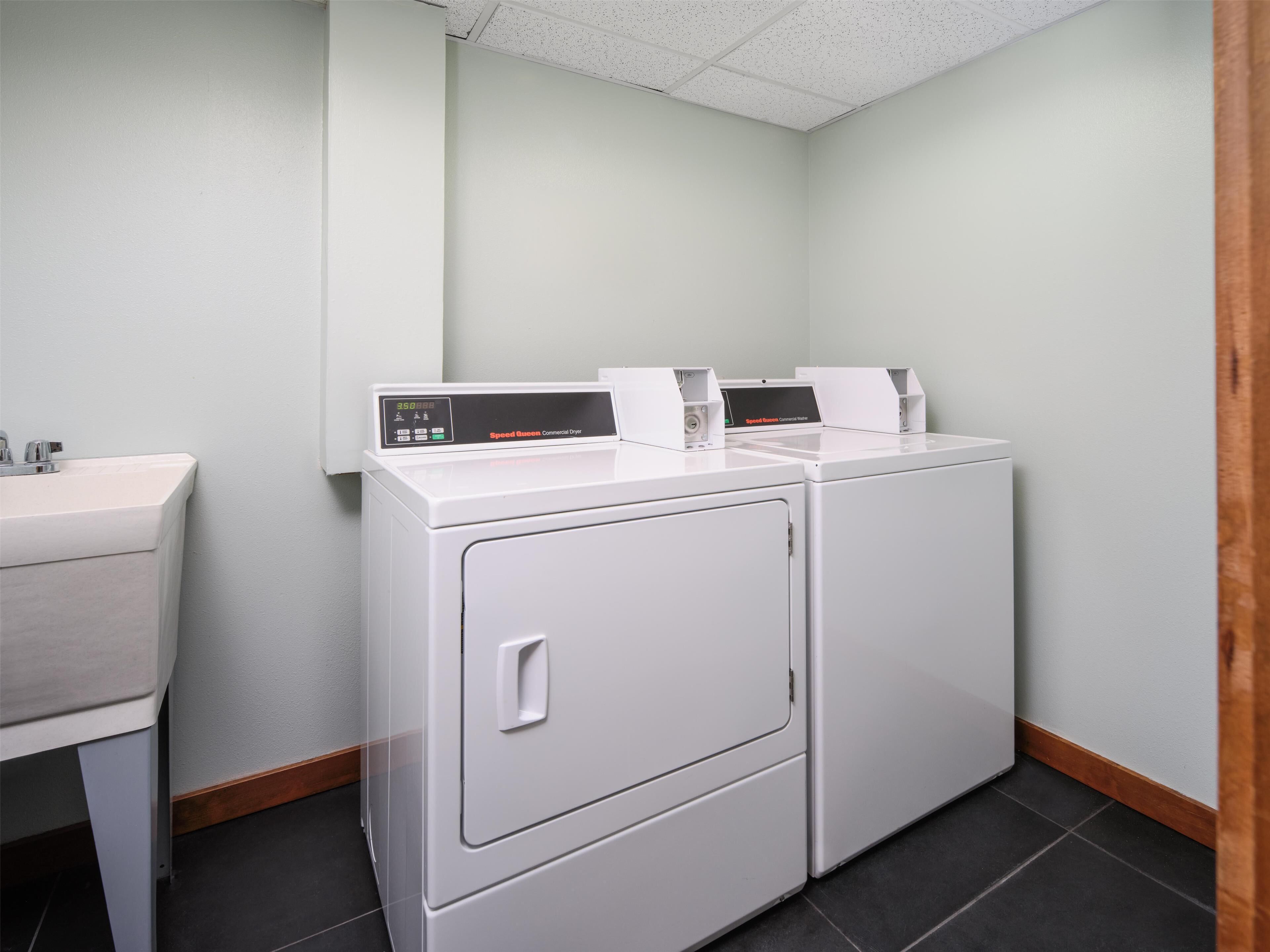 A laundry room with two white commercial dryers, a sink, and a wooden baseboard.