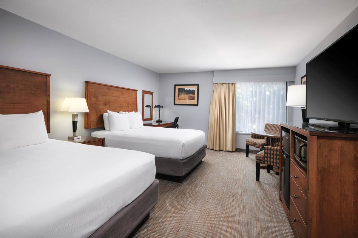 A hotel room with two beds, a TV, a desk, and a chair.