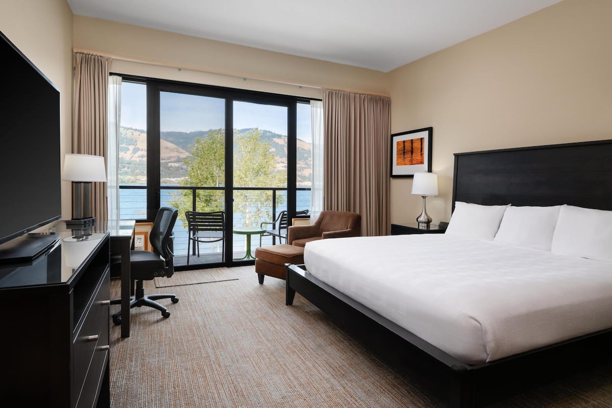 A hotel room with a large bed, a desk with a computer, a chair, and a TV.