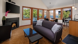 A modern living room with a fireplace, a sofa, a dining area, and large windows offering a view of the outdoors. - Best Western Plus Hood River Inn (Hood River)
