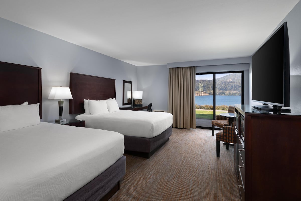 A hotel room with two beds, a TV, a desk, and a view of a lake.