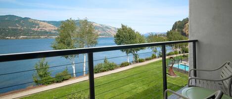 A balcony with a view of a lake and hills, a pool, and outdoor seating.