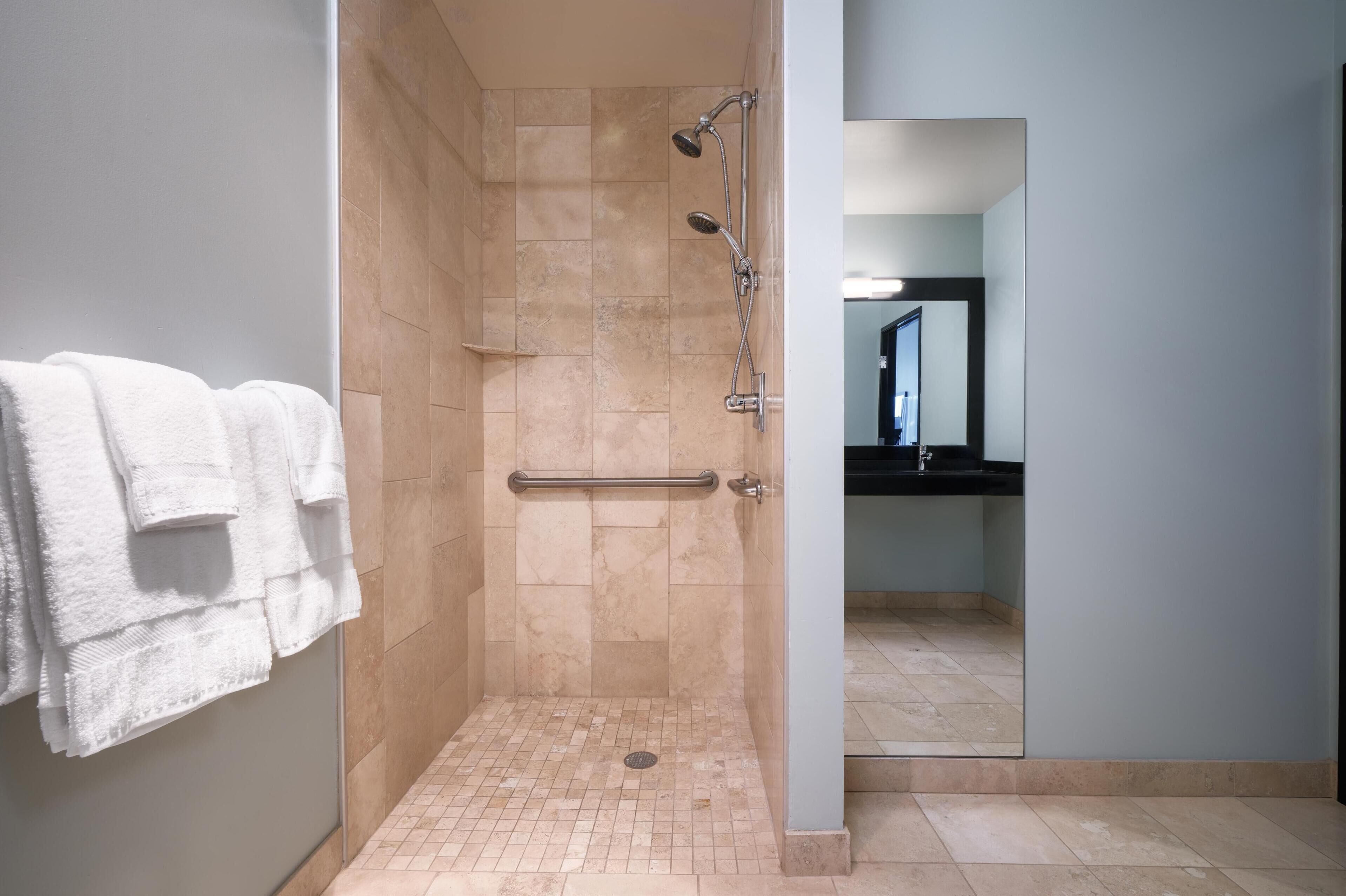 Une salle de bain moderne dotée d’une douche à l’italienne, d’une barre d’appui et d’un porte-serviettes avec des serviettes pliées.