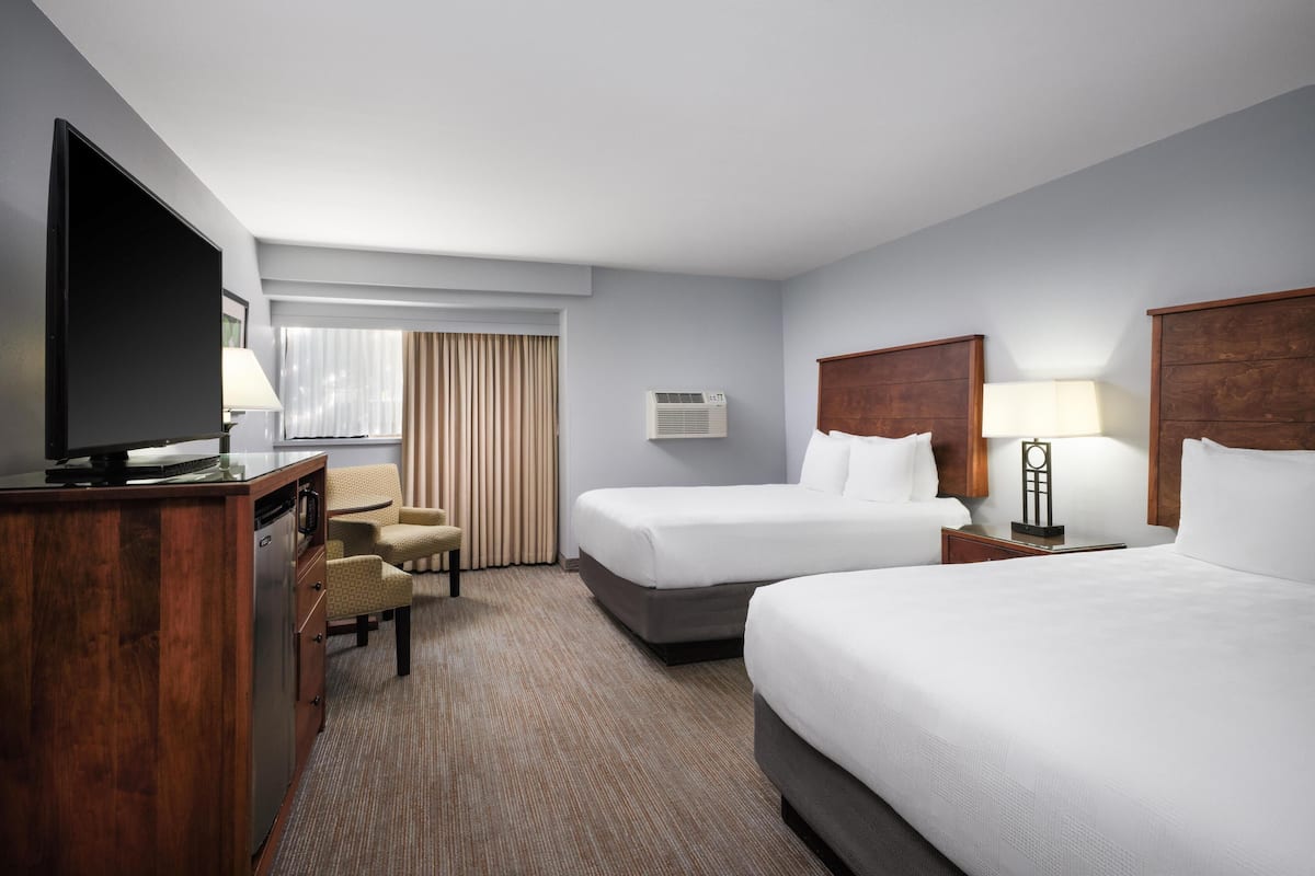 A hotel room with two beds, a desk with a television, a chair, and a window with curtains.