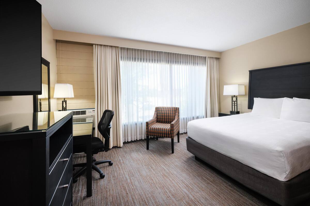 A hotel room with a large bed, a desk with a computer, a chair, and a TV.