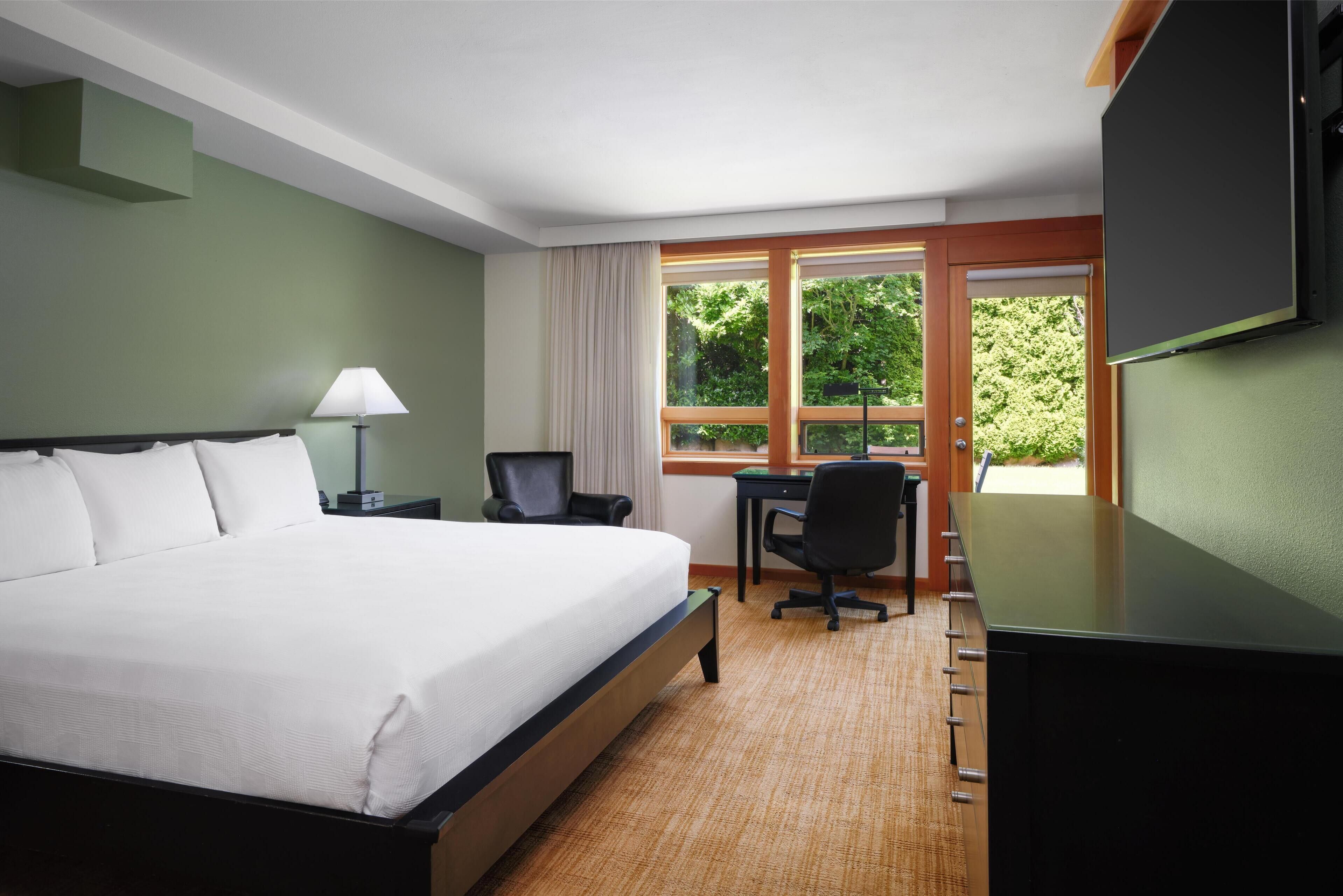 A hotel room with a large bed, a desk, a chair, and a TV.