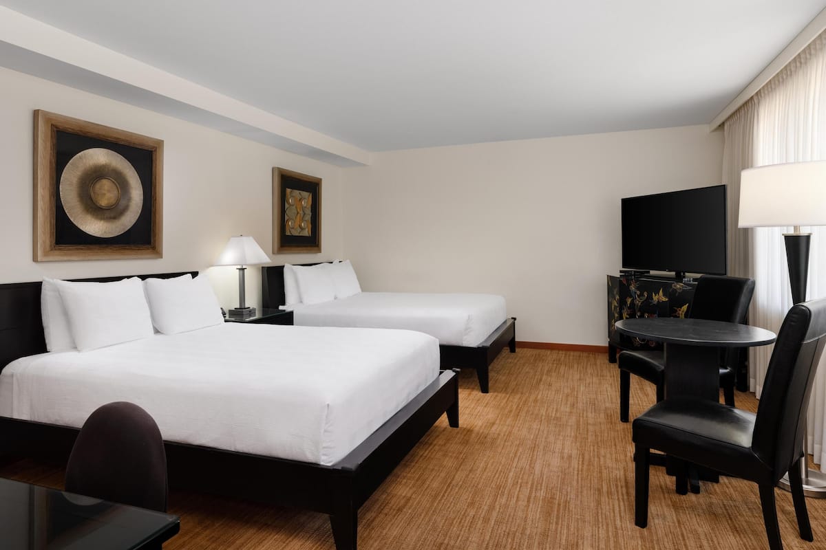 A hotel room with two beds, a desk, a chair, a TV, and a table.