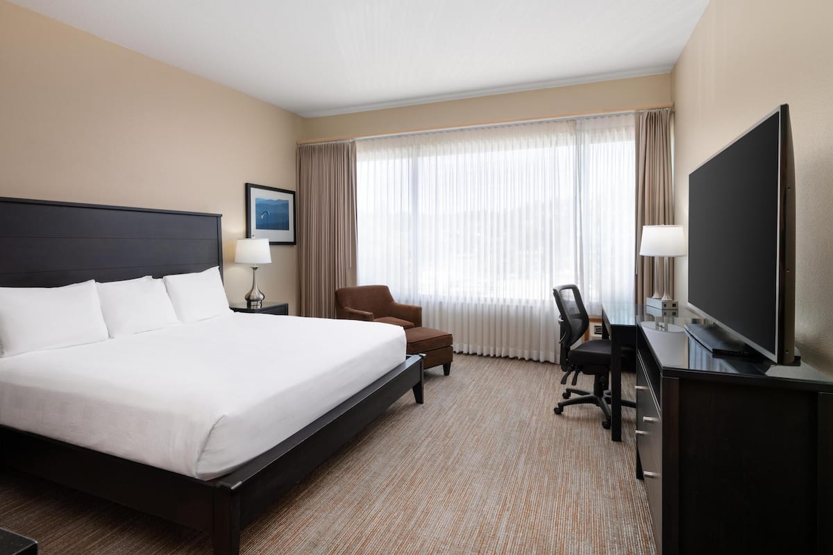 A hotel room with a large bed, a desk with a computer, a chair, and a TV.