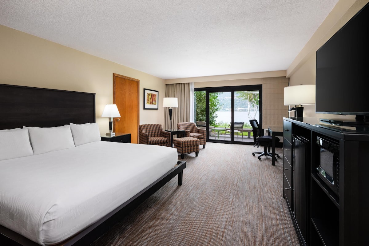 A hotel room with a large bed, a desk with a computer, a TV, and two chairs. There is a window with a view of the outdoors.