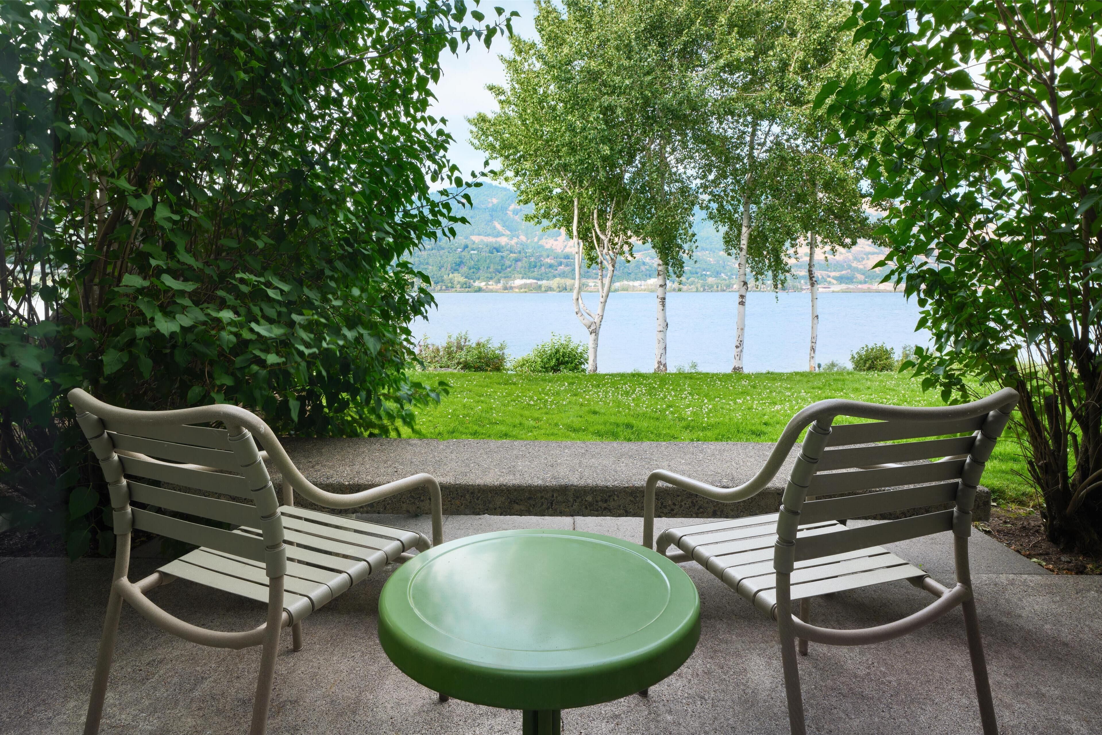 Un banco y una mesa sobre una superficie de concreto, con vista a un lago y árboles al fondo.