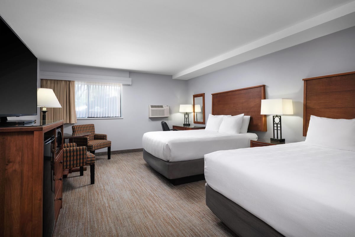 A hotel room with two beds, a desk with a TV, a chair, and a window with curtains.