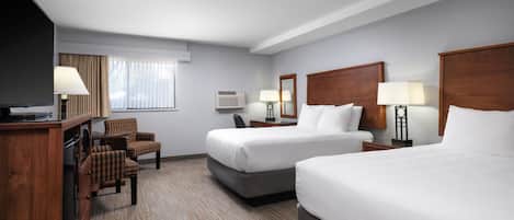 A hotel room with two beds, a desk with a TV, a chair, and a window with curtains.