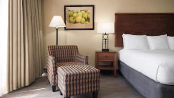 Une chambre d’hôtel avec un lit, une chaise, une table de chevet, une lampe et un tableau encadré au mur.