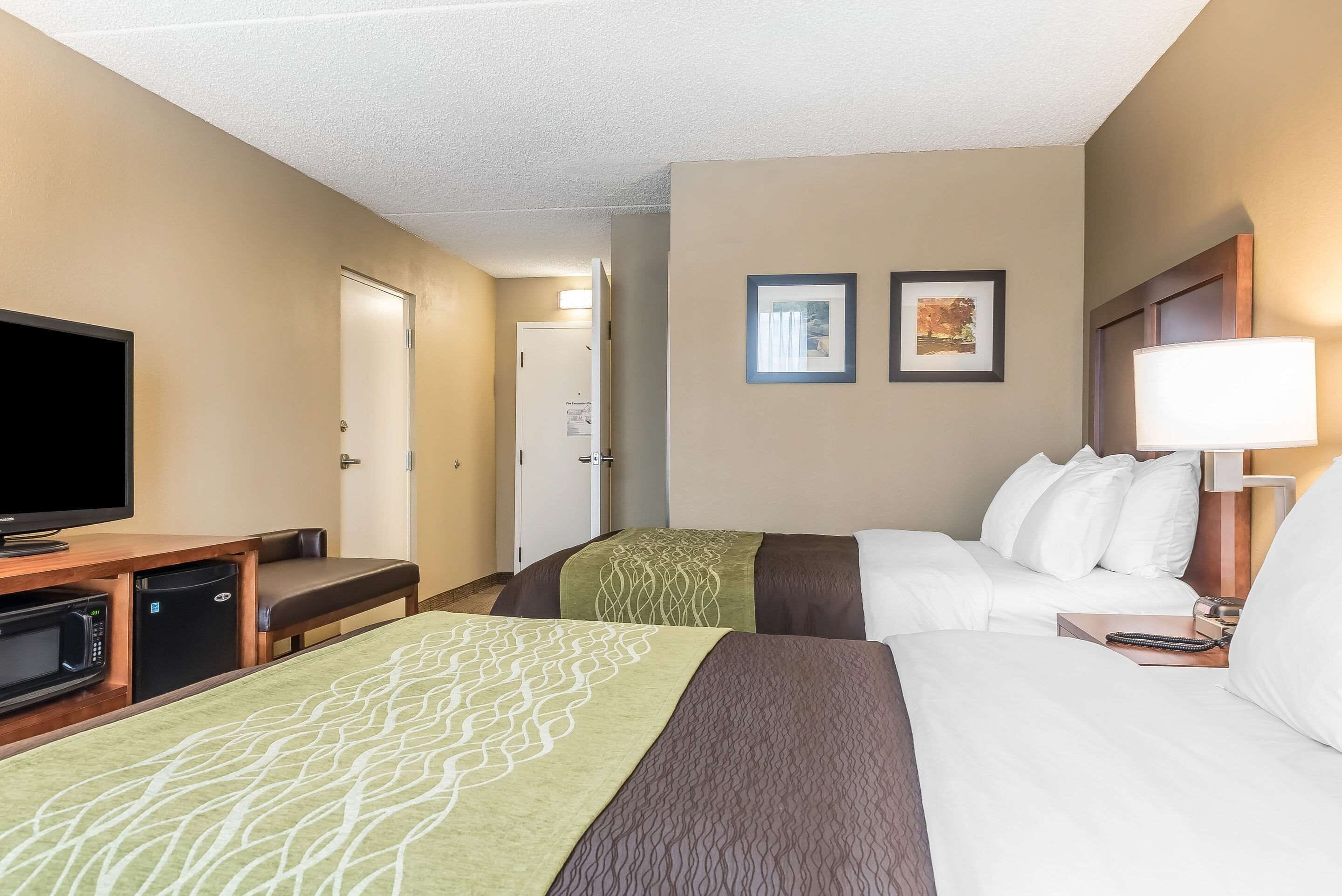 A hotel room with two beds, a television, a microwave, and a desk.