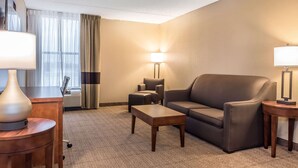 Quarto de hotel com sofá, poltrona e uma pequena mesa. Há uma luminária em uma mesa lateral e outra na parede.