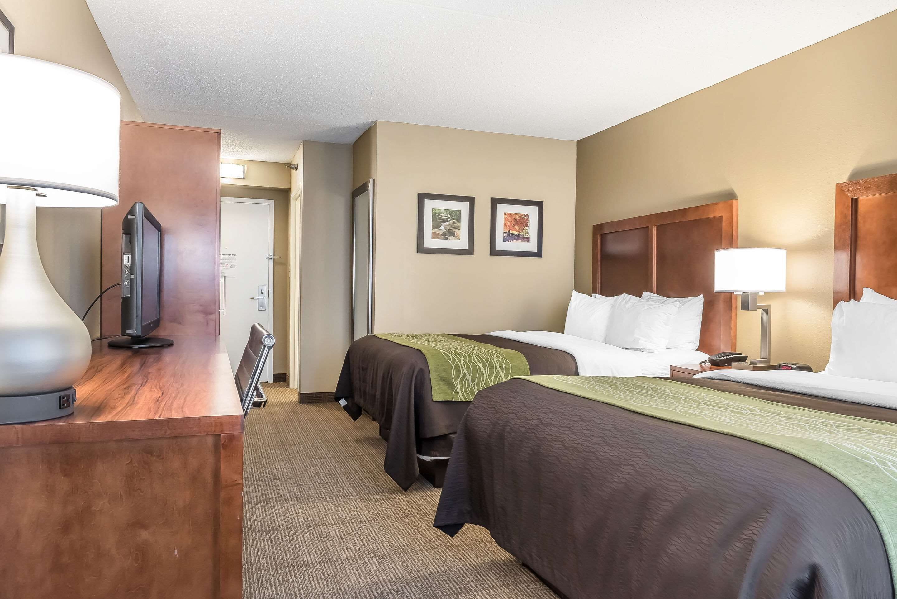A hotel room with two beds, a desk with a television, and a door leading to a bathroom.