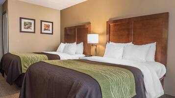 A hotel room with two beds, each with a wooden headboard, a bedside lamp, and a framed picture on the wall.