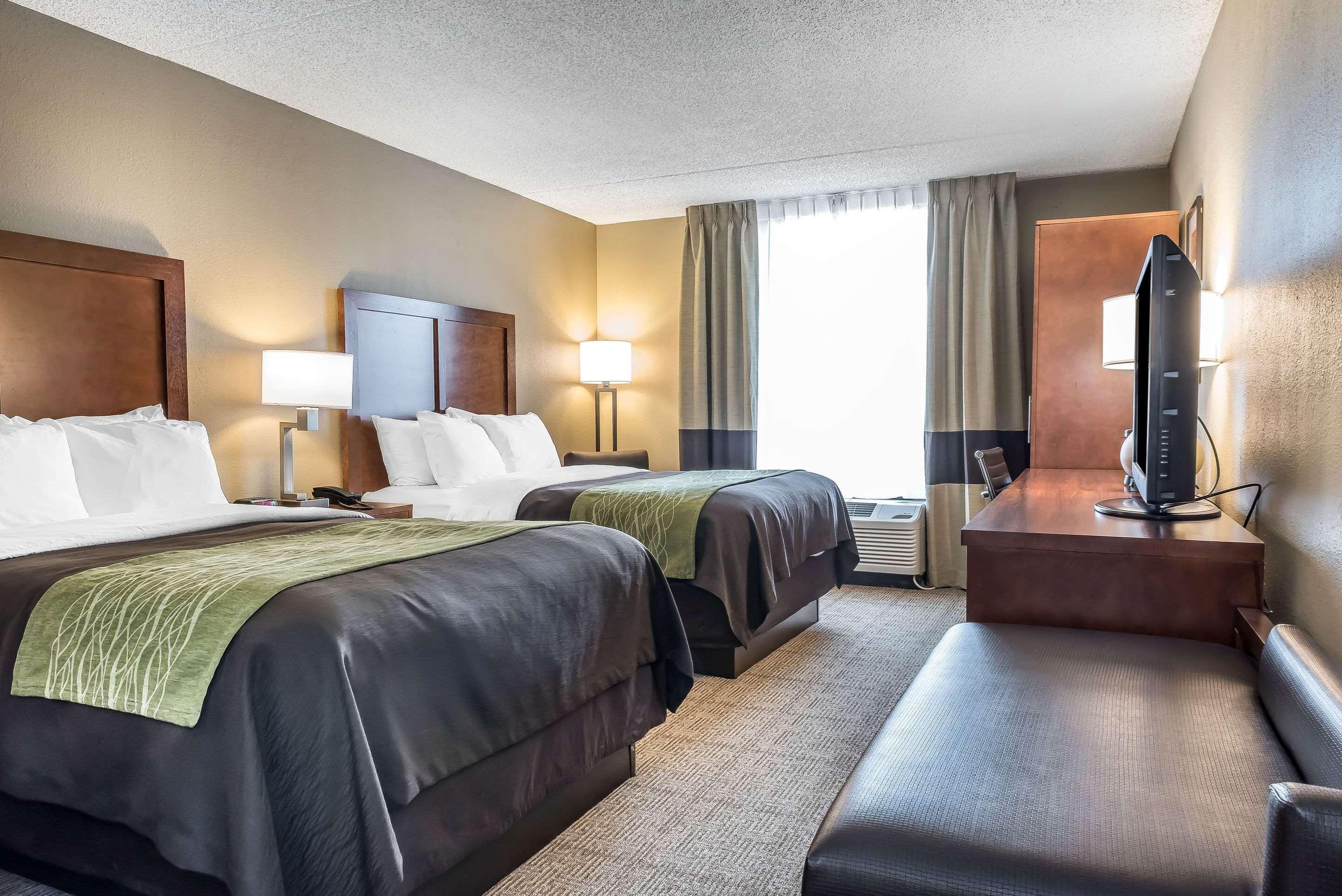 A hotel room with two beds, a desk with a computer, a TV, and a window with curtains.