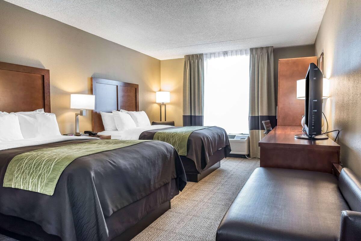 A hotel room with two beds, a desk with a television, and a seating area.