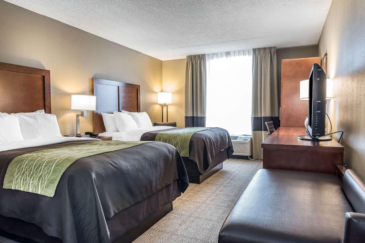 A hotel room with two beds, a desk with a computer, a TV, and a window with curtains.