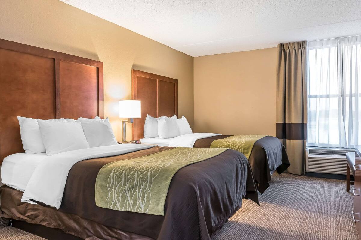 A hotel room with two beds, a desk, a lamp, and a window with curtains.