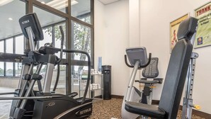 Uma academia com equipamentos de cardio, aparelhos de musculação e um cartaz fixado na parede.