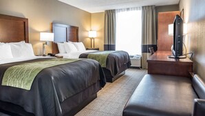 Quarto de hotel com duas camas, uma escrivaninha, televisão e janela com cortinas.