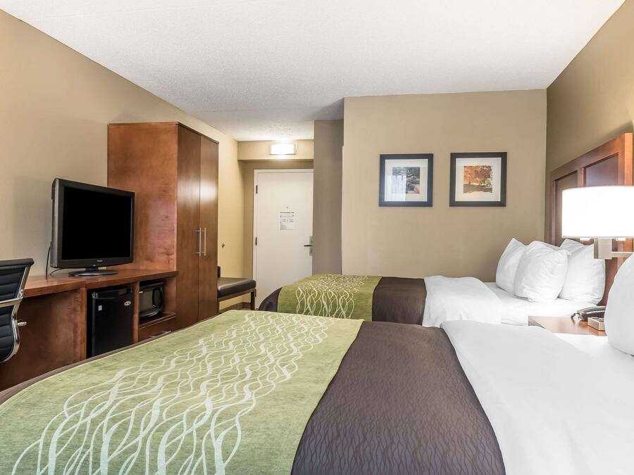 Une chambre d’hôtel avec deux lits, un bureau avec une télévision, un minibar et une porte donnant sur un couloir.