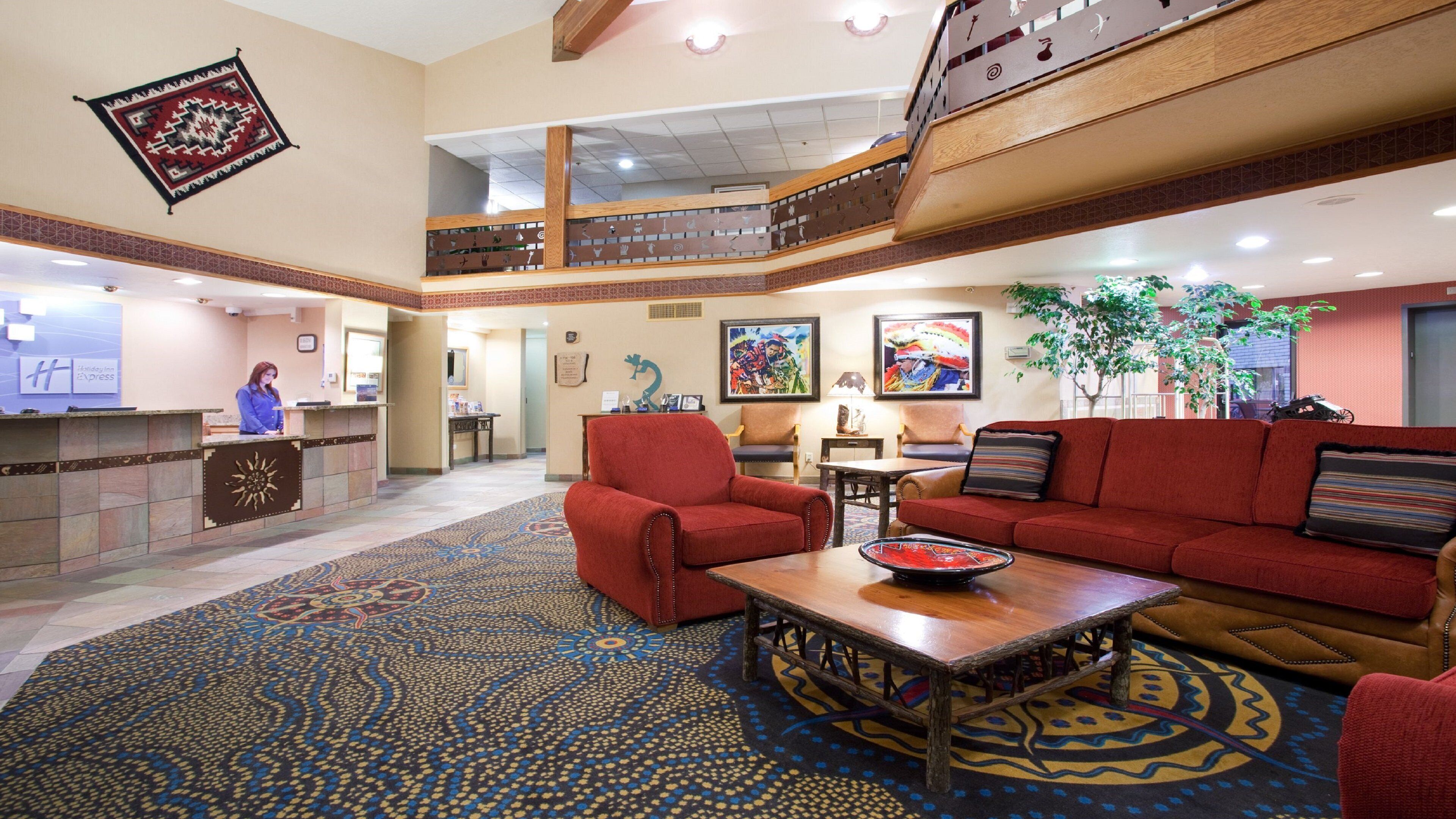 A hotel lobby with a reception desk, red seating, a coffee table, and a staircase.