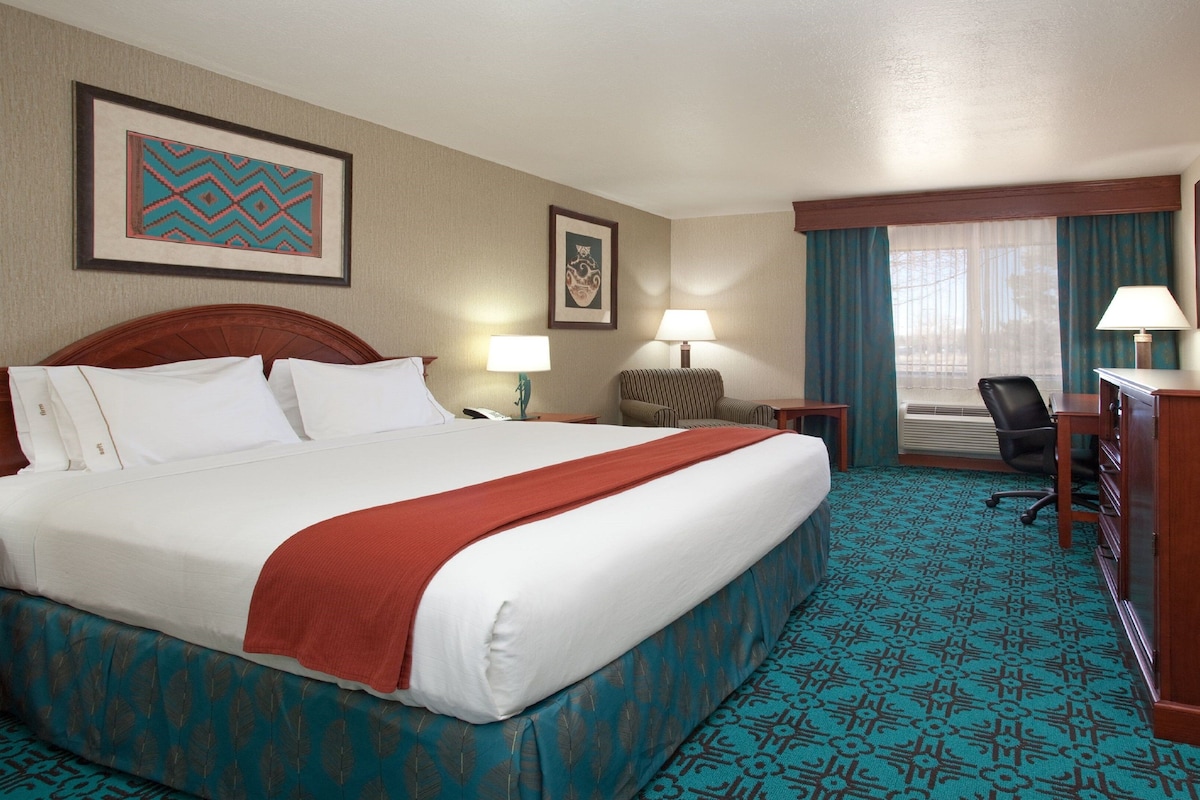 A hotel room with a large bed, a desk, a chair, a lamp, a television, and a window with curtains.
